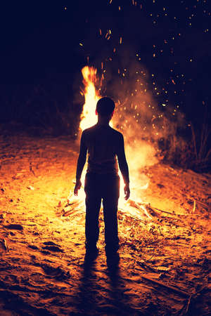 Young boy stand near a bright bonfireの写真素材