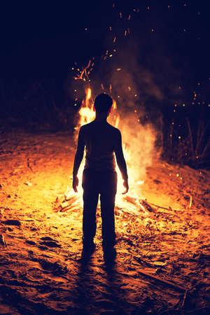 Young boy stand near a bright bonfireの写真素材