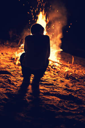 Young boy sit near a bright bonfireの写真素材