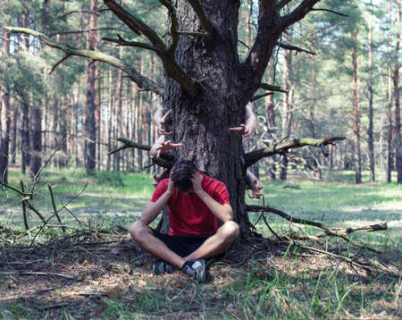 The young boy sits in fear under a treeの写真素材