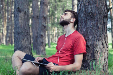 The boy sits under a tree and listens to musicの写真素材