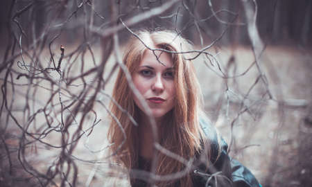 Beautiful girl in forest between dry branchesの写真素材