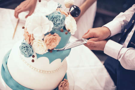 The groom cuts beautiful and tall wedding cakeの写真素材