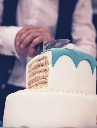 The groom cuts beautiful and tall wedding cakeの写真素材