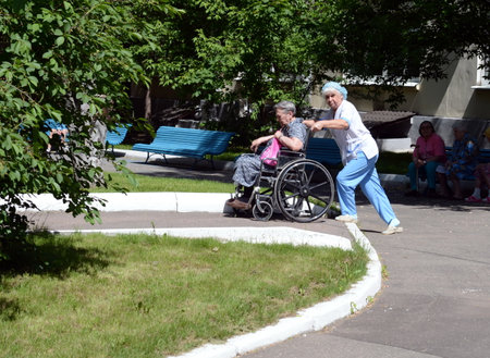 The nurse is rolling an elderly woman in a wheelchair on the territory of the hospital of veterans of wars.のeditorial素材