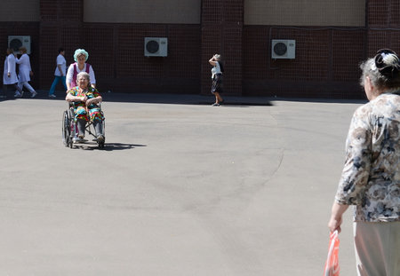 The nurse is rolling an elderly woman in a wheelchair on the territory of the hospital of veterans of wars.のeditorial素材