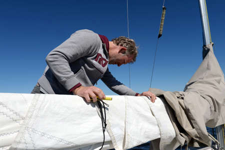 Unknown yachtsman makes minor repairs to the sail on a yacht