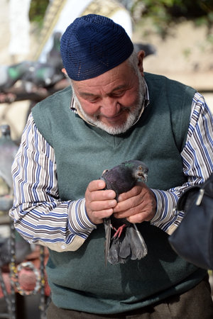 An unknown elderly man holds a pigeon in his hands on a street in Istanbulのeditorial素材