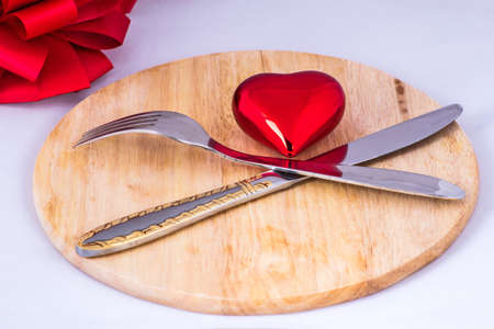 Beautiful toy heart lies on a chopping board. Nearby are the fork and knife.の写真素材