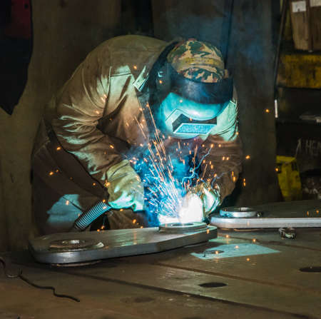 Welder at work in the blinding light of bright splashes of red-hot metal  