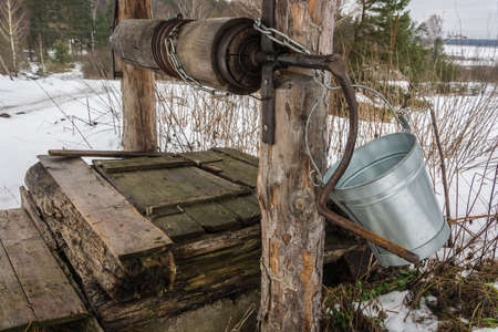 The old wooden well on the edge of the village with a metal bucket for water lifting  の写真素材