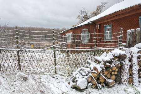 Polenitsa firewood in the courtyard of the village houses covered with snow. On the metal wires of the fence are visible ice icicles.の写真素材