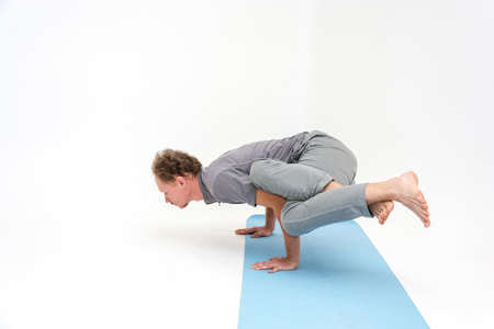 Man performs asanas of Hatha yoga on a blue mat and white background.