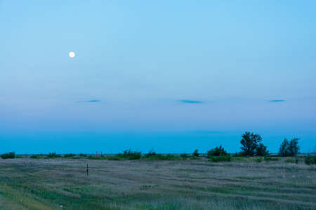 Bright white moon on blue sky background in the steppe area.の写真素材