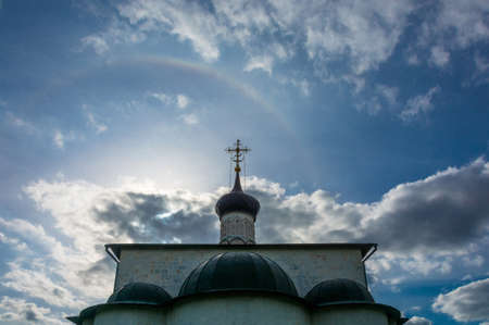 Beautiful Church steeple with a gold cross on a background cloudy sky decorated with rainbow.の写真素材