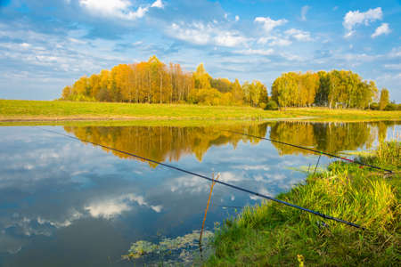 Beautiful river autumn landscape in a Sunny day with fishing rods.の写真素材