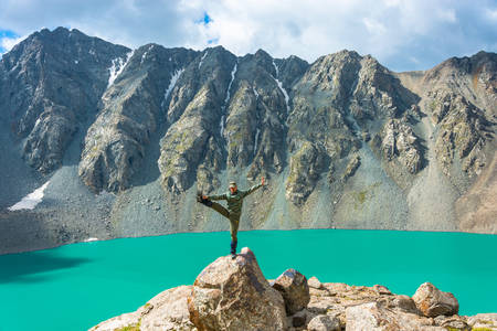 A man standing on a huge rock performs the asanas on the background of a mountain lake Ala-Kul, Kyrgyzstan.の写真素材