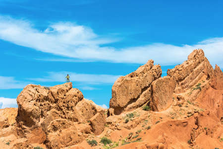 A man stands on a huge rock against the blue sky in the canyon Fairy Tale, Kyrgyzstan.の写真素材