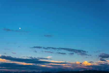 Blue sky with bright clouds, illuminated by the setting sun.の写真素材