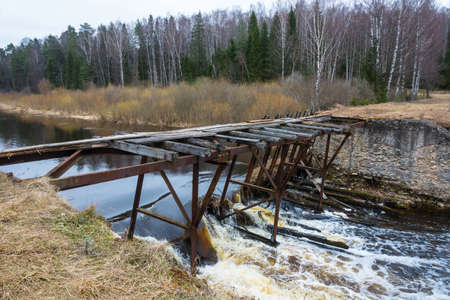 The dilapidated bridge over the small tumultuous river on a cloudy April day.の写真素材