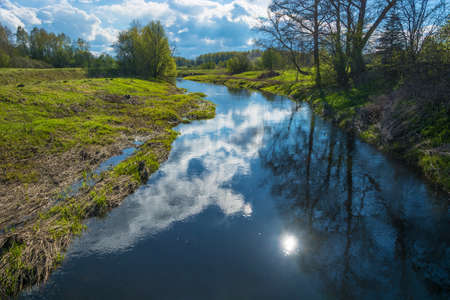 Beautiful spring landscape with reflection of sun and clouds in the water of a small river.の写真素材