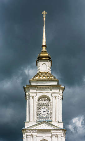 High gold Church steeple with a clock on the background of a stormy sky.の写真素材