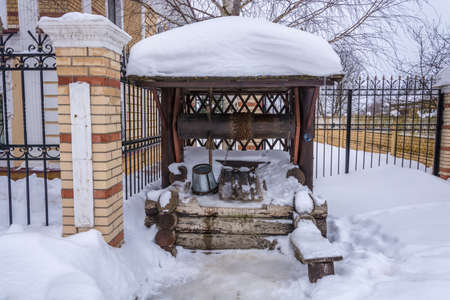 A wooden well with a metal bucket and chain on a winter day.の写真素材