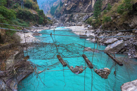 Old destroyed suspension bridge over the stormy mountain river in the Himalayas, Nepal.