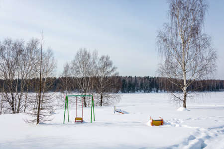 Playground with swings, covered with snow on a Sunny winter day.