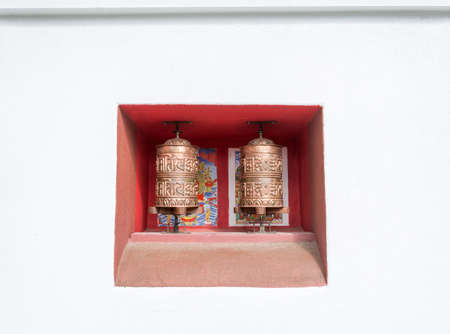 Two copper Buddhist prayer drums on red background in white wall.の写真素材