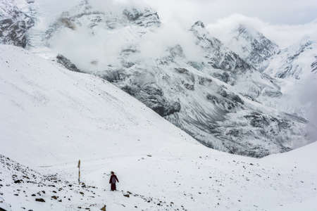 A lone monk on the snow-covered Thorong La pass on a cloudy day, Nepal.