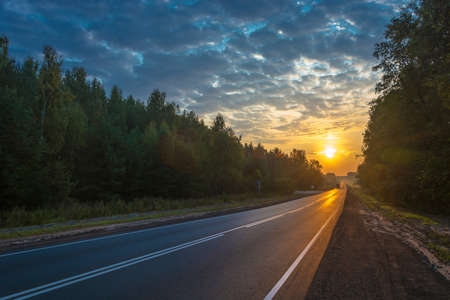 Asphalt road in the bright rays of the rising sun with a beautiful cloudy sky.の写真素材