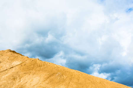 A large mountain of yellow sand, illuminated by the sun against the cloudy sky.の写真素材