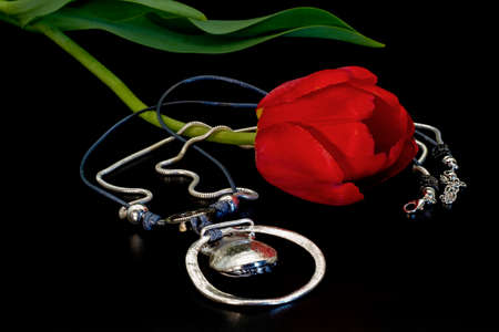 Silver pendant-pendant on blue and silver lace and a red tulip with green leaves on a black background.の写真素材