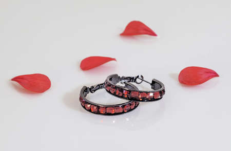 Two dark round earrings with bright red stones and red flower petals on a light background.の写真素材