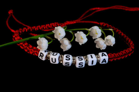 Red lace charm bracelet and white lily of the valley flower on a black background.の写真素材