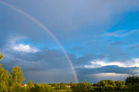 A multicolor rainbow against a dark cloudy sky on a summer day, Russia.の写真素材