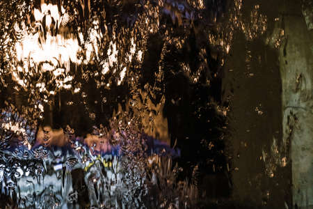 Bright multi-colored abstraction: water flowing down the glass with the reflection of night lights.