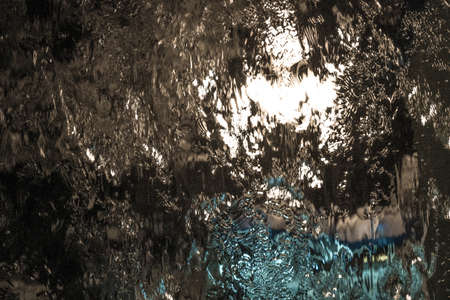 Bright multi-colored abstraction: water flowing down the glass with the reflection of night lights.