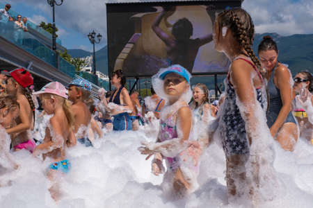 Yalta, Crimea - 07/09/2019: Children in snow-white foam on the beach on a sunny day.のeditorial素材