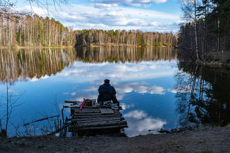 Fisherman on a log pier against the background of the forest and a beautiful reflection of the...