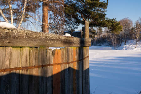 The corner of an old wooden fence in the sunlight of the winter sun, Russia.の写真素材