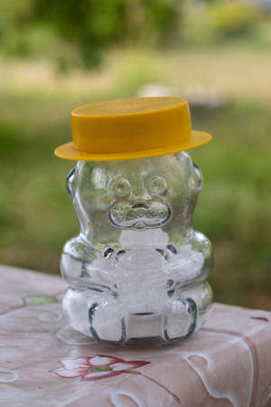 A glass salt shaker in the shape of a bear in a yellow hat, standing on the edge of the table on a blurry background.の写真素材