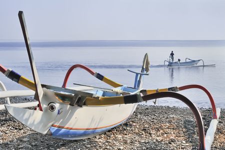 Traditional Balinese fishing boat and fisherman on calm early morning seaの写真素材