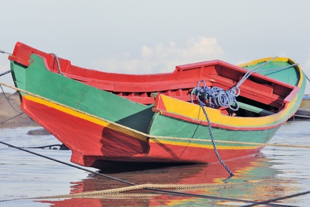 Brightly colored indonesian fishing boat on beach at low tideの写真素材