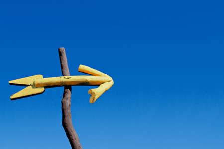 An arrow sign hand made of wood, painted yellow, hanging on the branch の写真素材