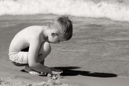 Sad, lonely boy on the beach playing with the sand の写真素材
