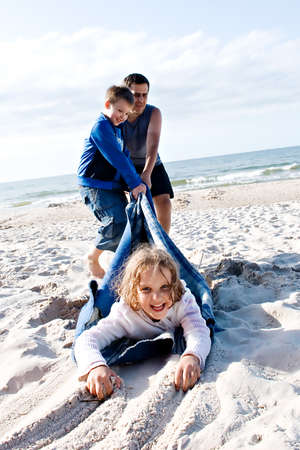 Happy family  father with son and daughter  having fun on the beach while pulling spontaneously on the sand during vacation の写真素材