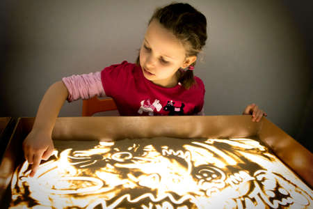 Child girl draws with sand on a light table.の写真素材