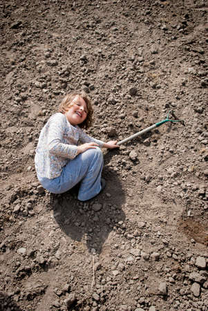 Girl laying on soil with hoe in her hand, having funny time.の写真素材